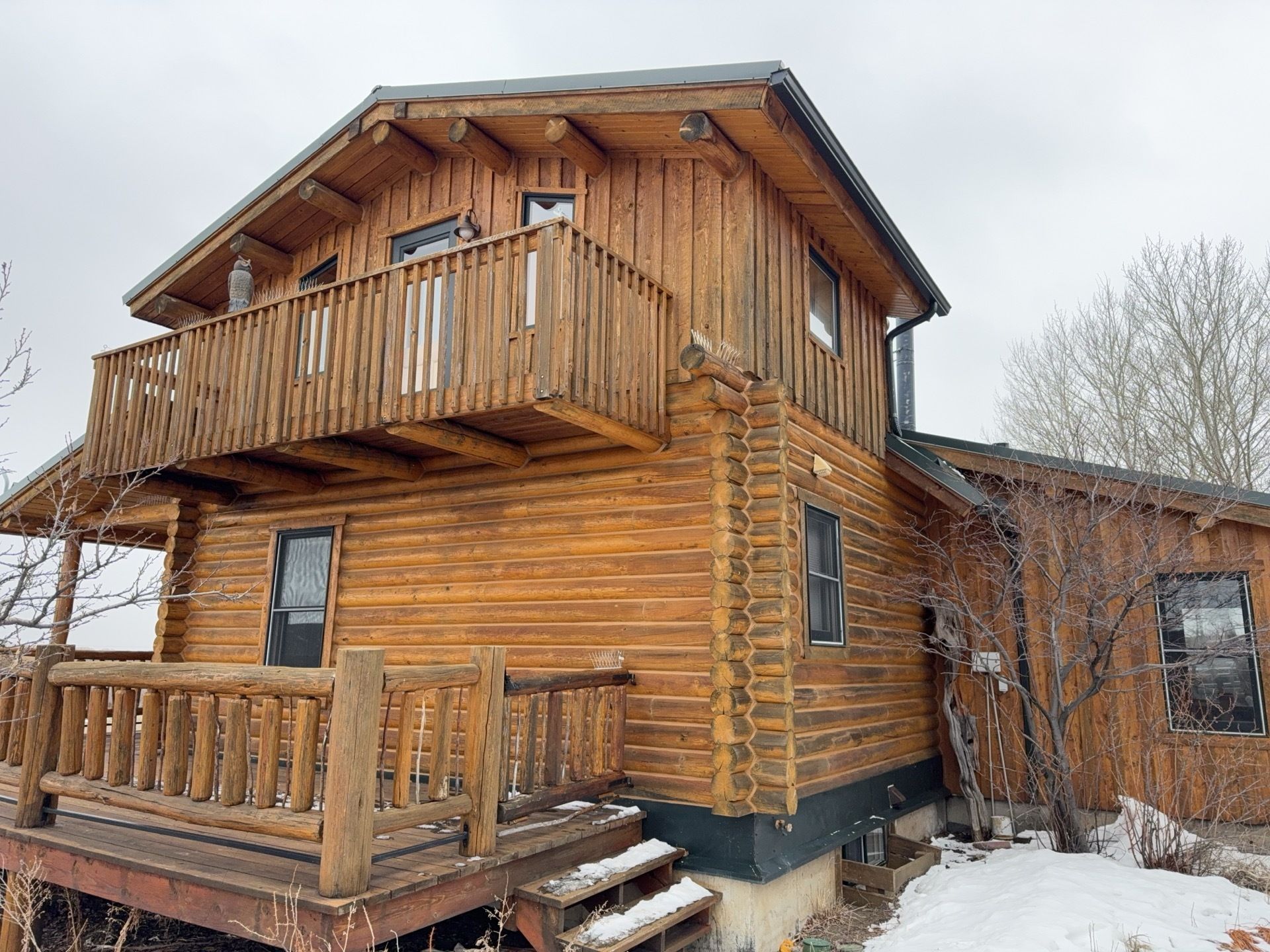 Wooden log cabin with a white SUV parked beside it under a clear blue sky