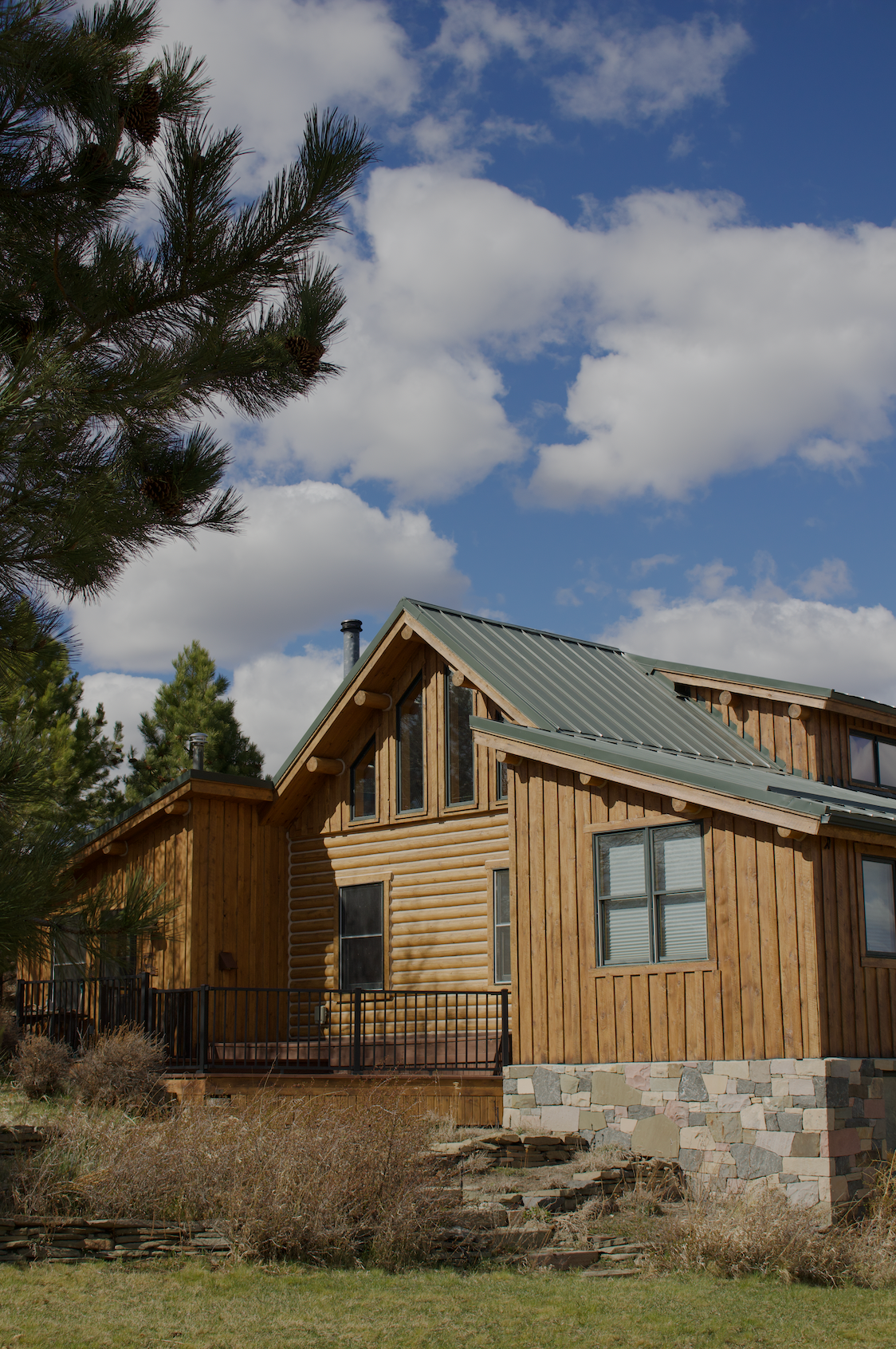 Wooden cabin with green roof and stone foundation under a cloudy blue sky