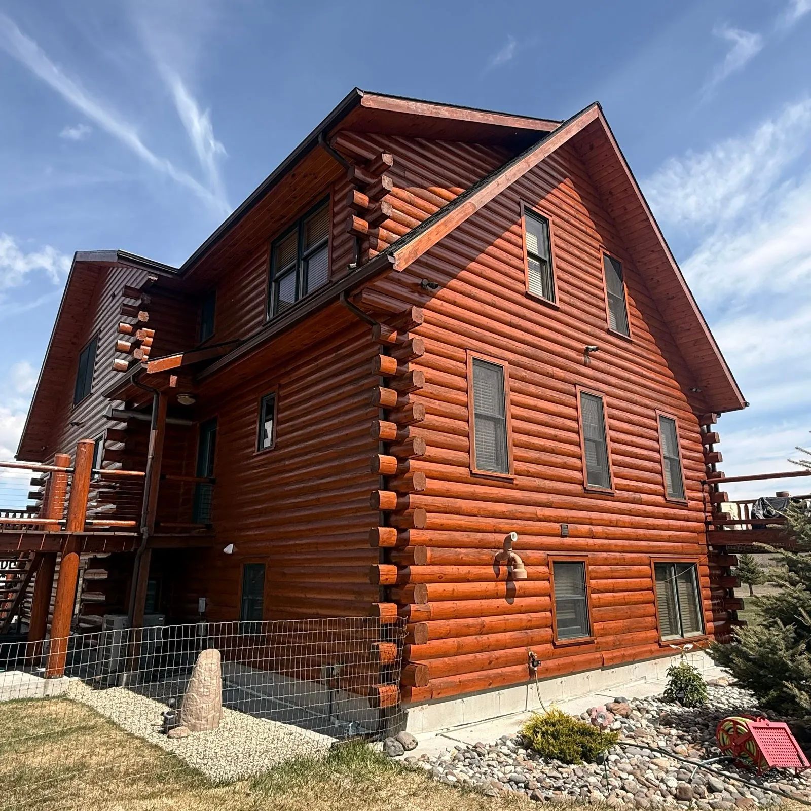 Red log house with multiple windows under a blue sky, viewed from the corner