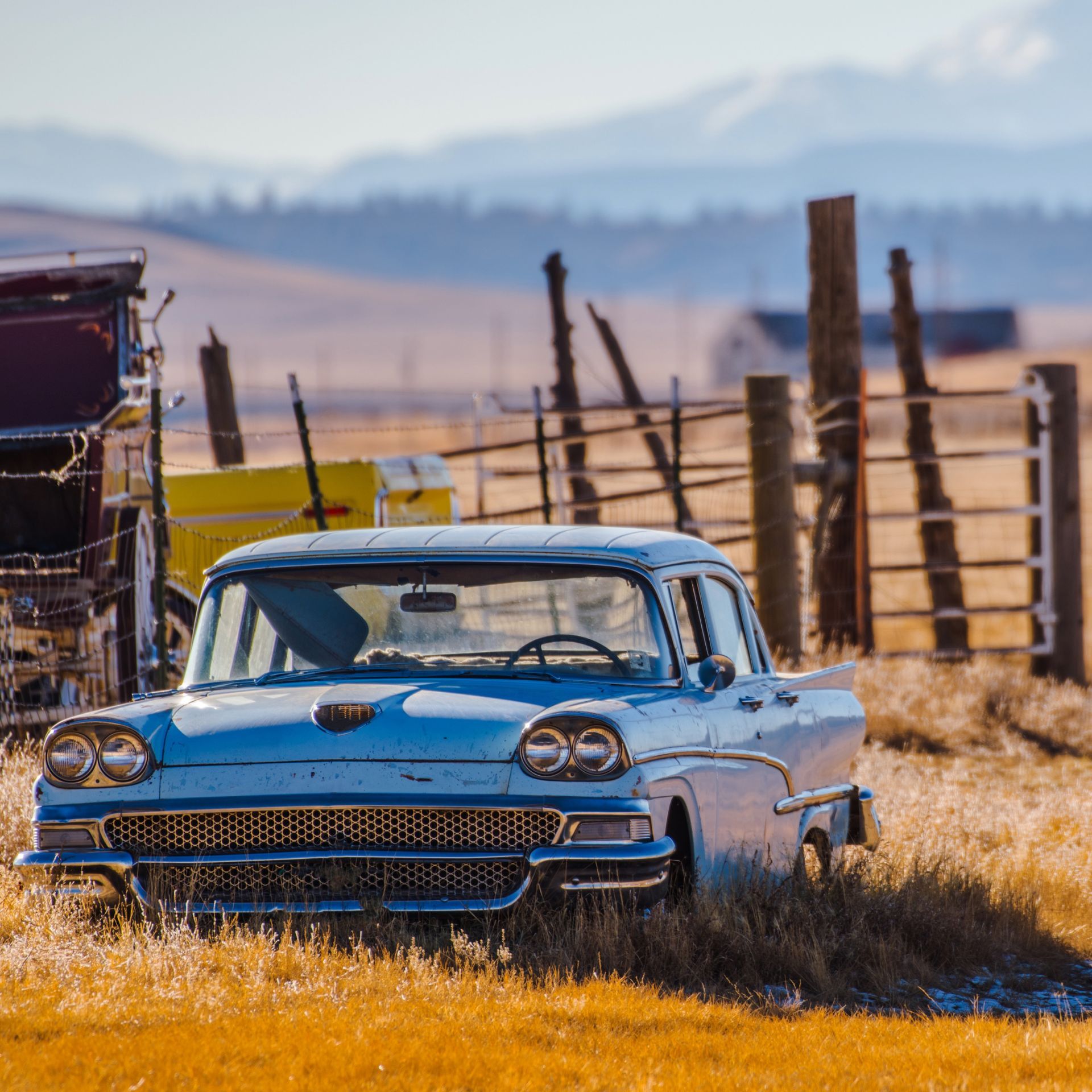 A blue car is parked in a field next to a fence