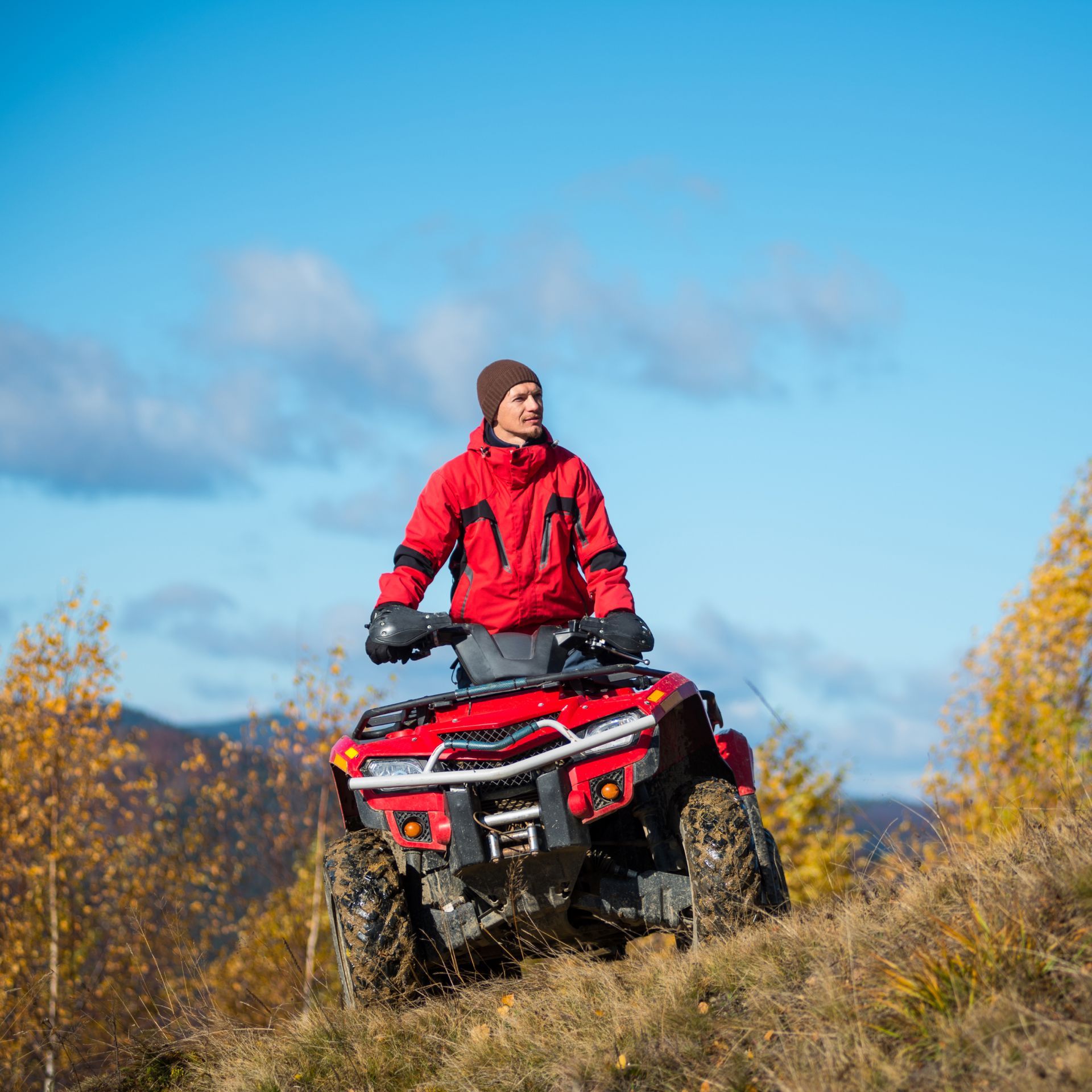A man in a red jacket is riding a red atv on top of a hill.