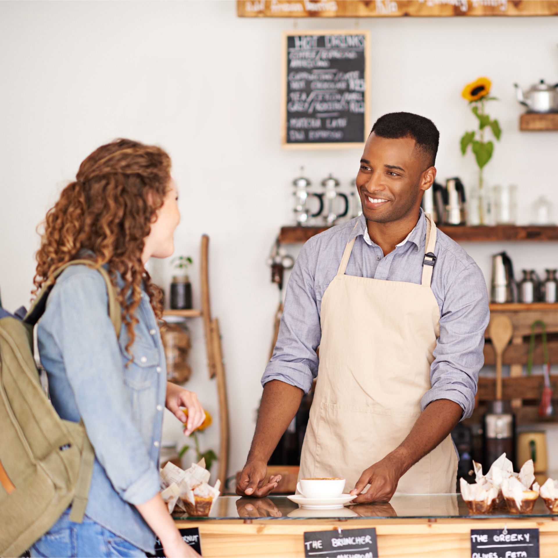 A man in an apron is serving a cup of coffee to a woman