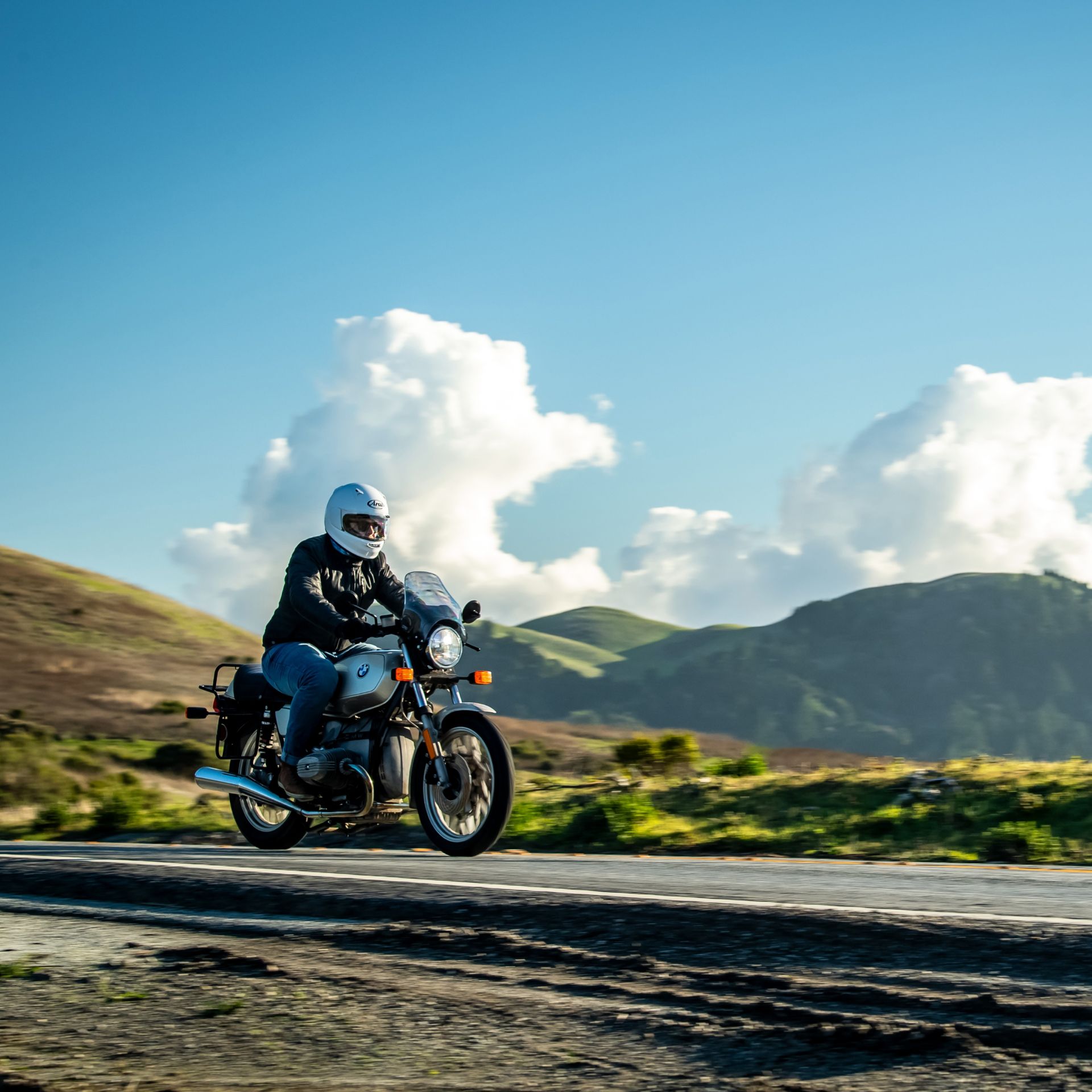 A man is riding a motorcycle down a road with mountains in the background.