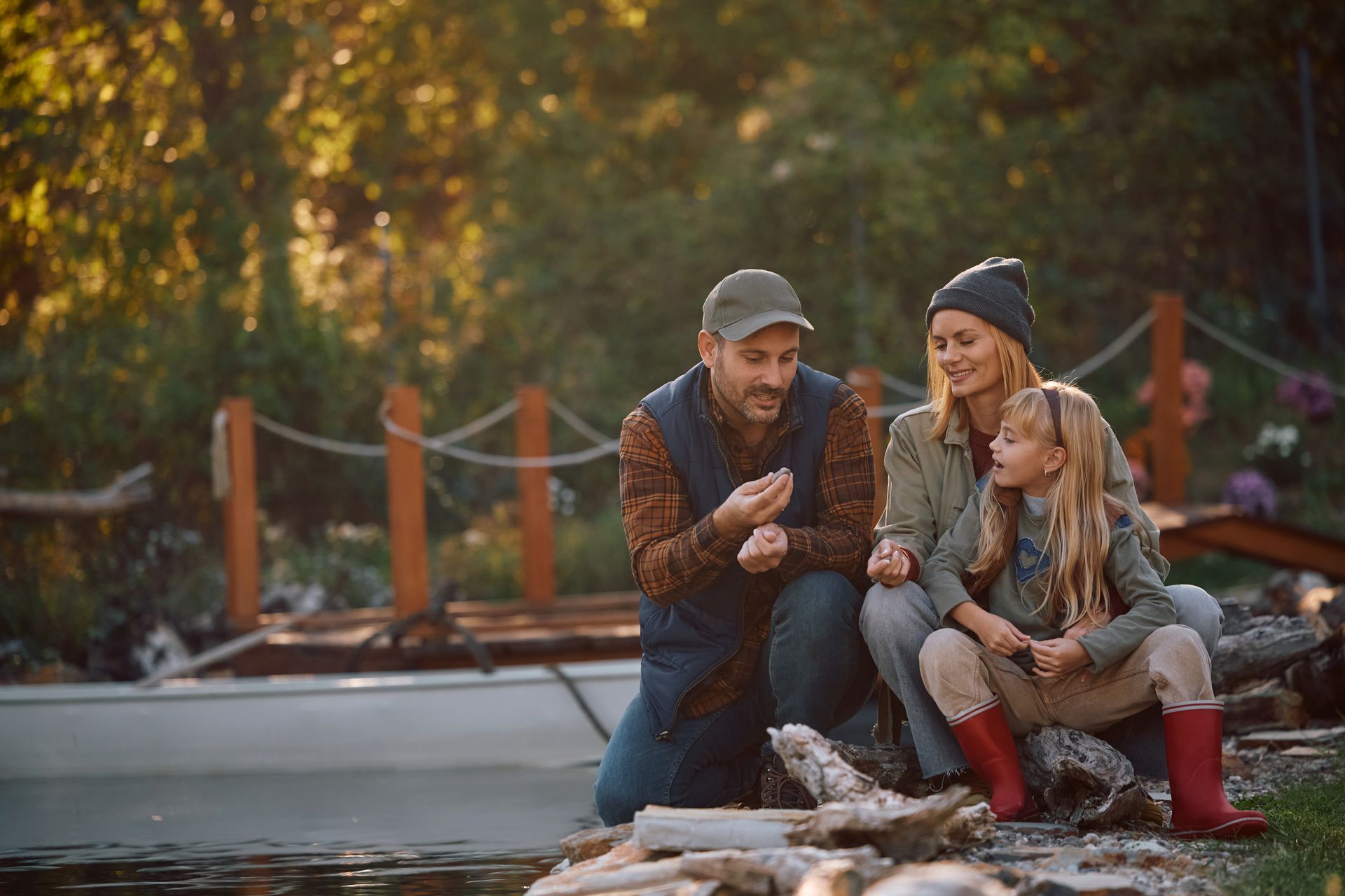A family is sitting around a campfire on the shore of a lake.