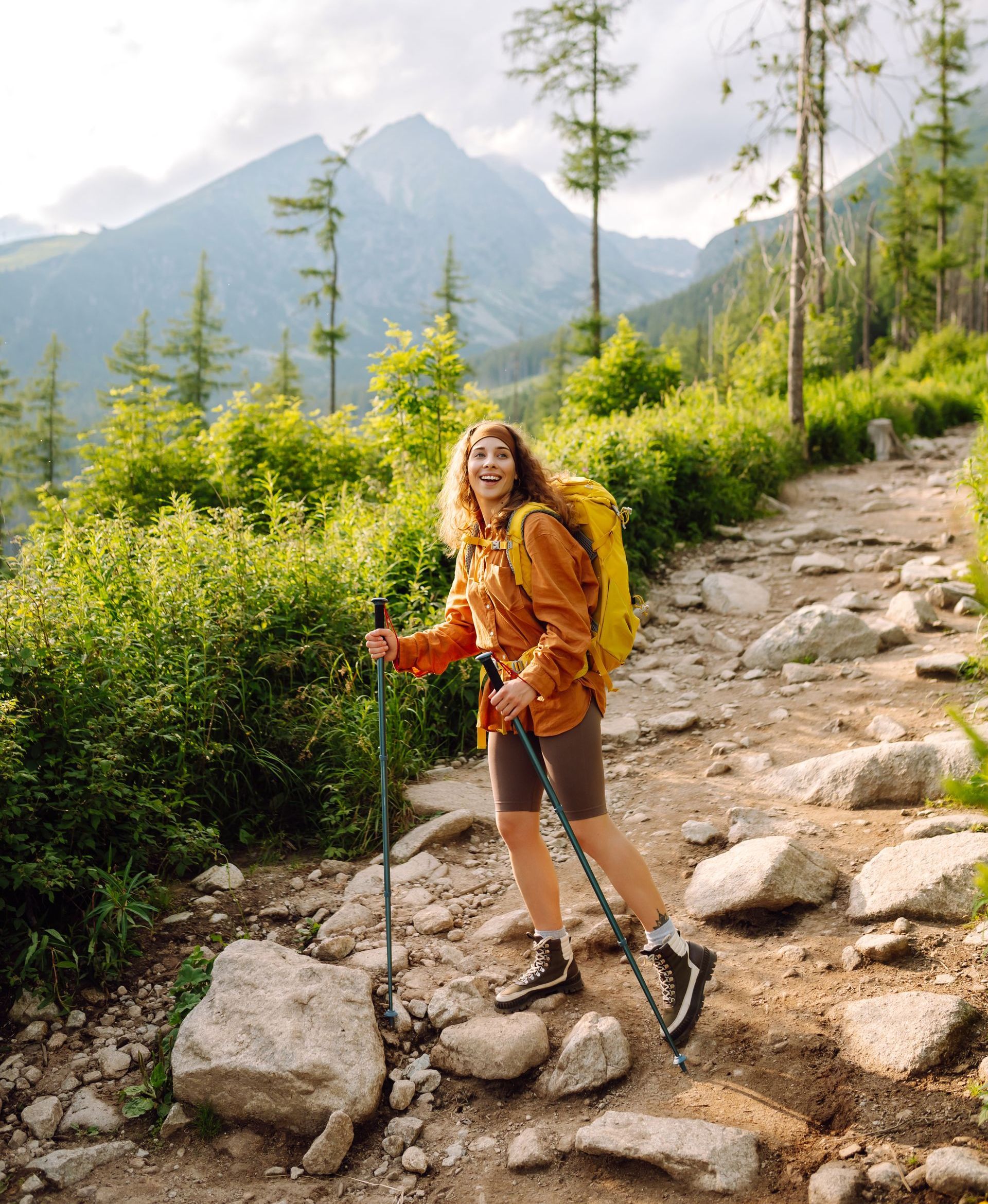 A woman with a backpack is hiking on a rocky trail in the mountains.