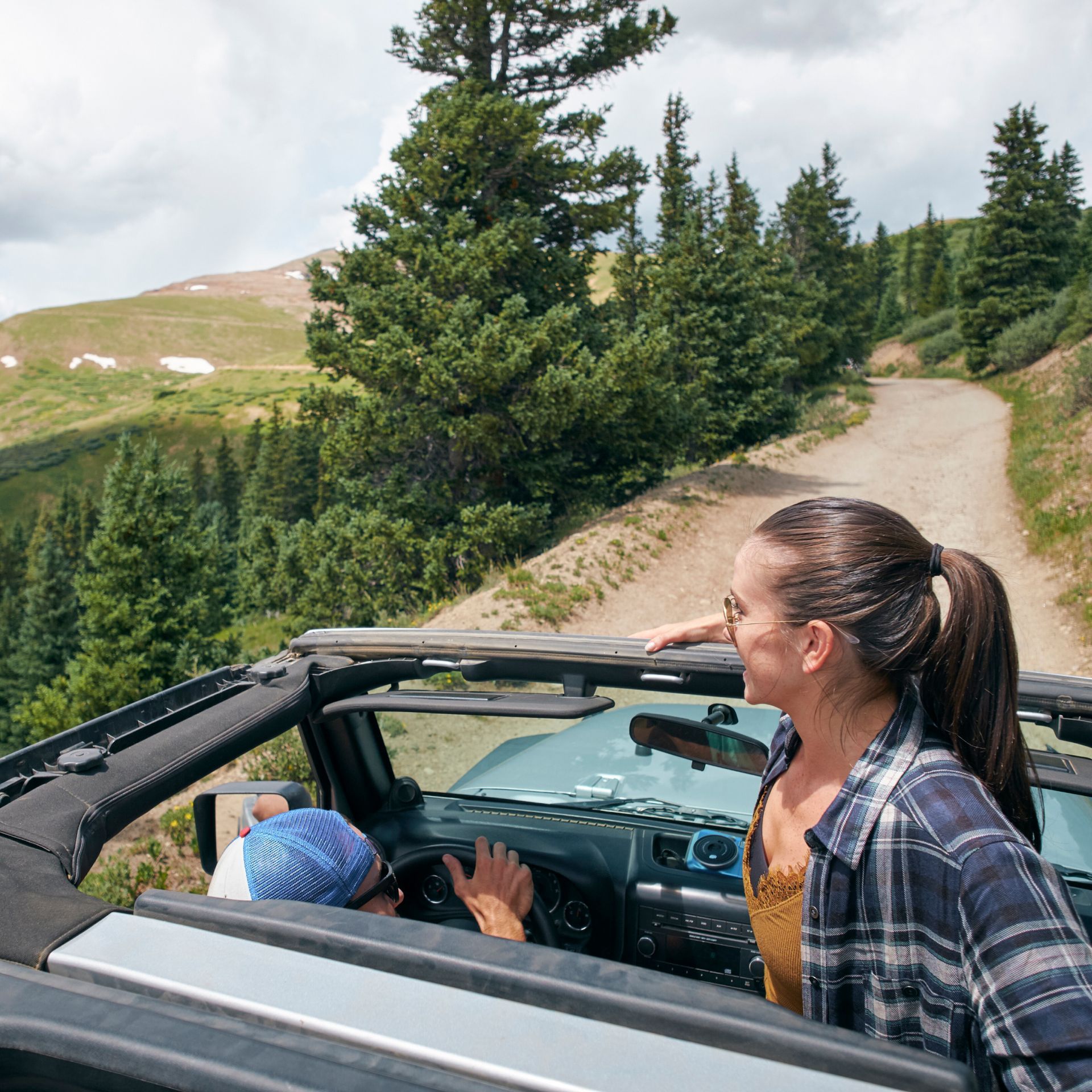 A man and a woman are driving down a dirt road in a convertible car.