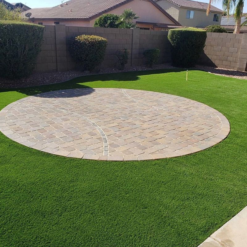 Backyard lawn with a large circular paved patio and brick wall fence