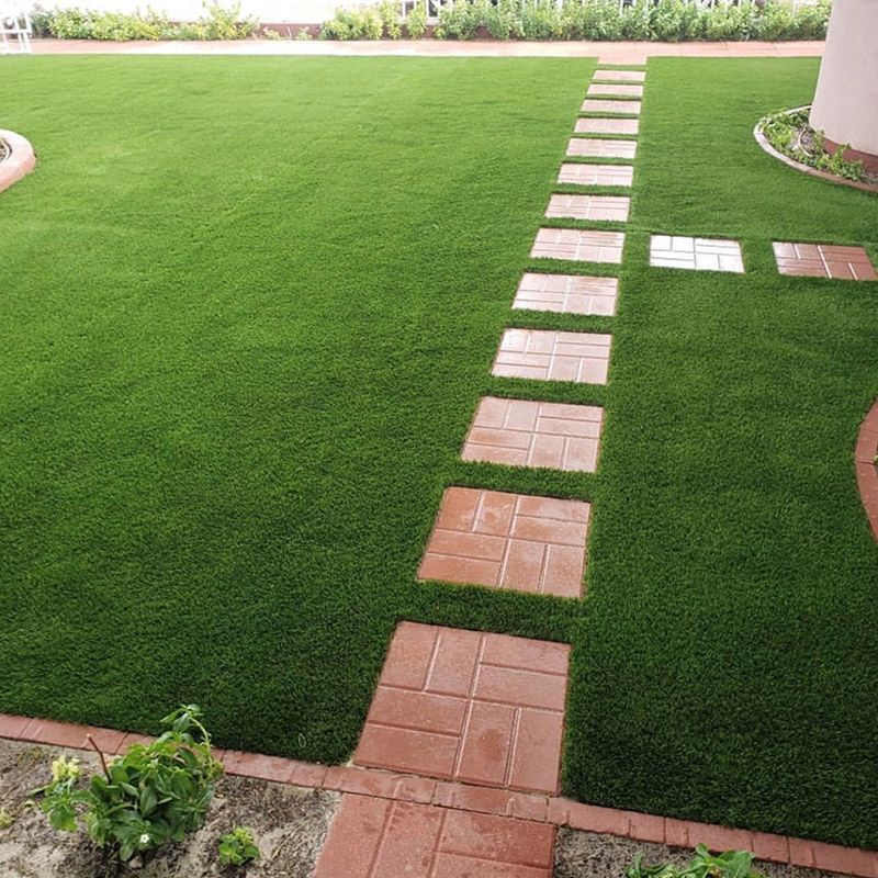 Camino de losas sobre un césped verde que conduce a un patio pavimentado.