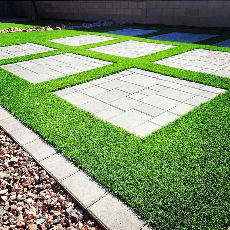 Modern patio with white pavers set in bright green artificial grass and a pebble border