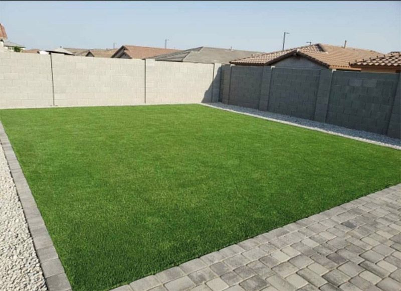 Patio trasero con césped verde, terraza pavimentada y muros altos que brindan privacidad bajo un cielo despejado