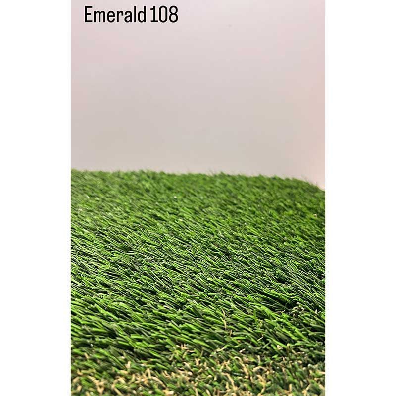 Césped artificial verde esmeralda con un fondo de pared clara y el texto “Emerald 108” en la parte superior izquierda