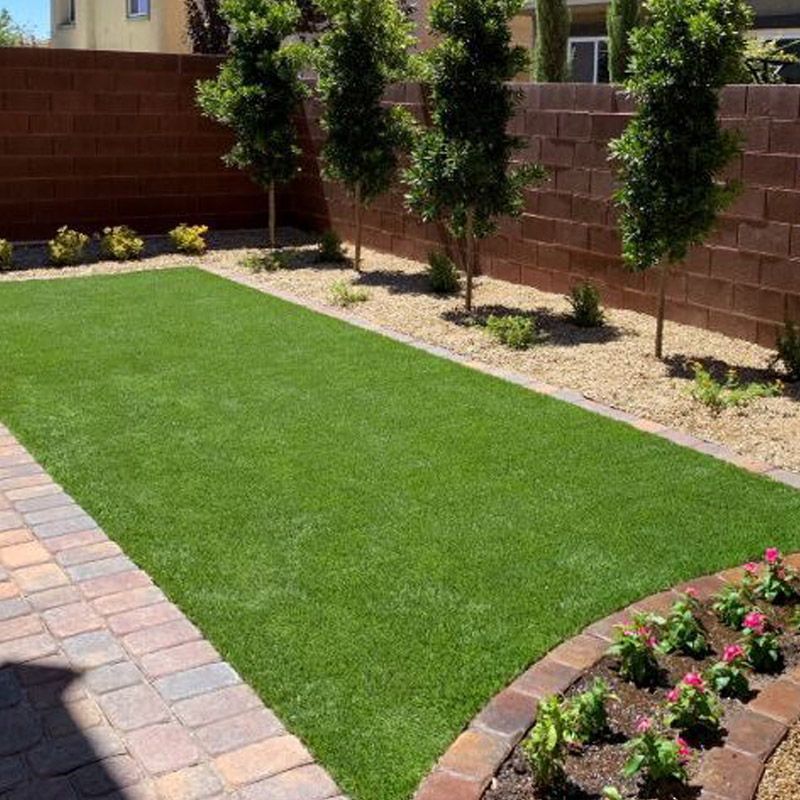 Landscaped backyard with green turf, brick path, stone border, and flowering plants along a wall