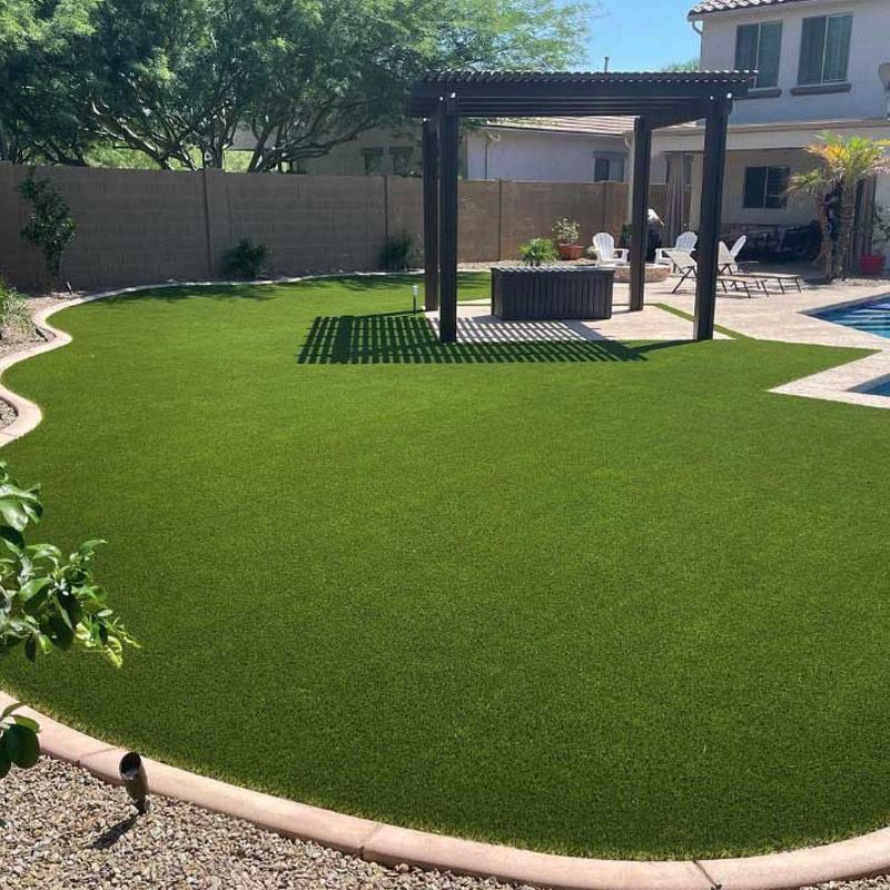 Backyard with lush green lawn, curved border, pergola, and patio beside a house