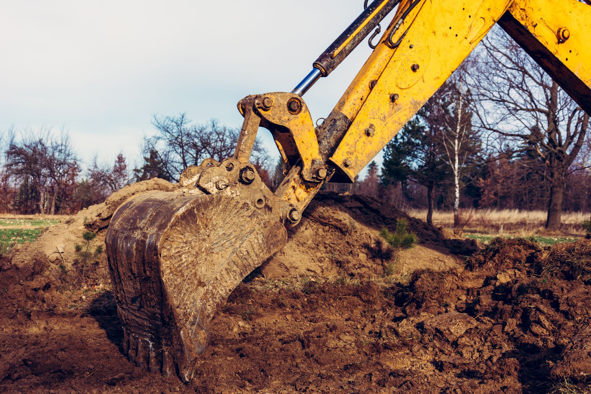 A yellow excavator is digging a hole in a field.