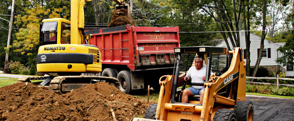 A man is driving a bulldozer next to a dump truck.