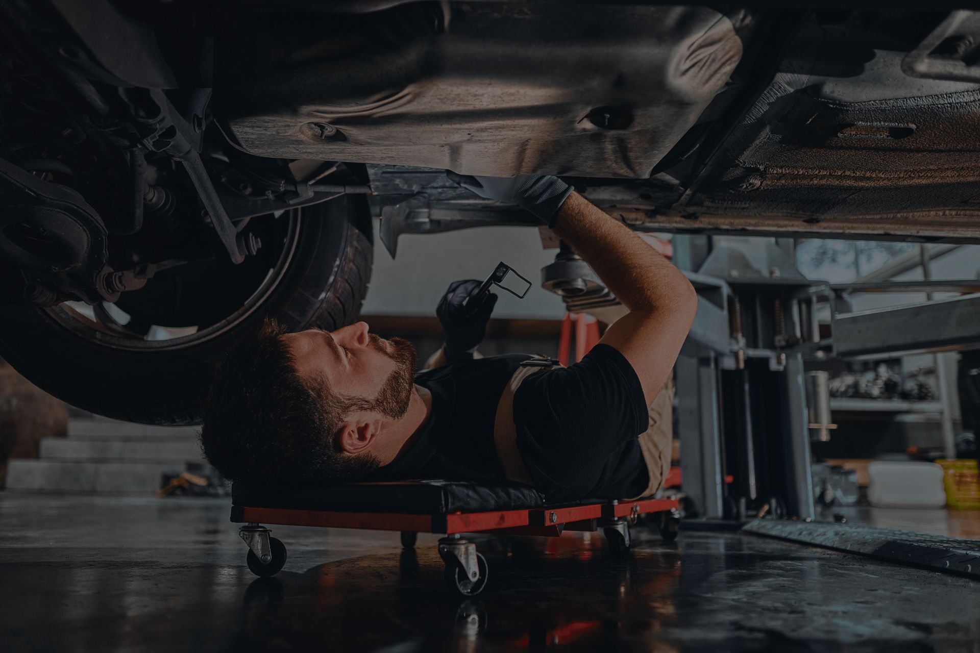 Mechanic working under a car, lying on a creeper. They are using a tool in a garage. | Integrated Automotive