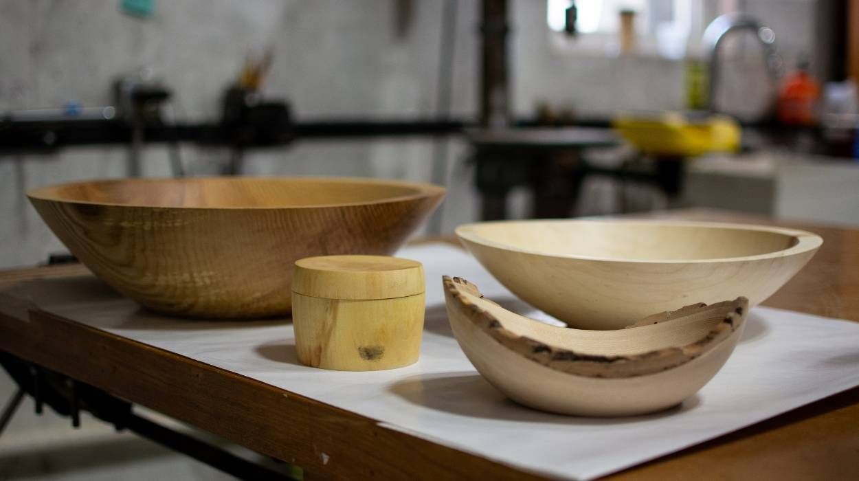 Three wooden bowls and a small lidded container sit on a white surface in a woodworking shop.