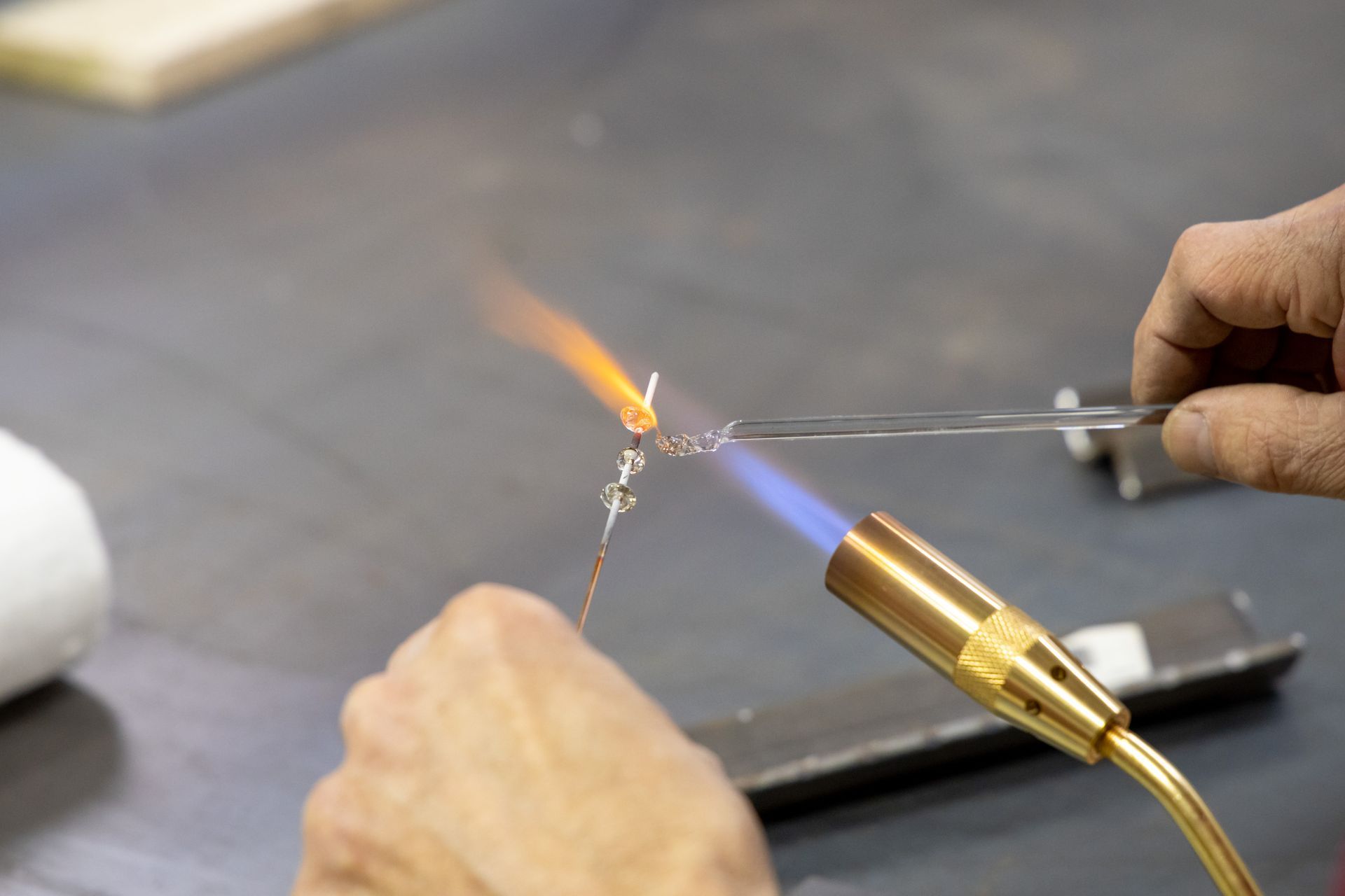 A person using a torch to melt and shape glass on a workbench.