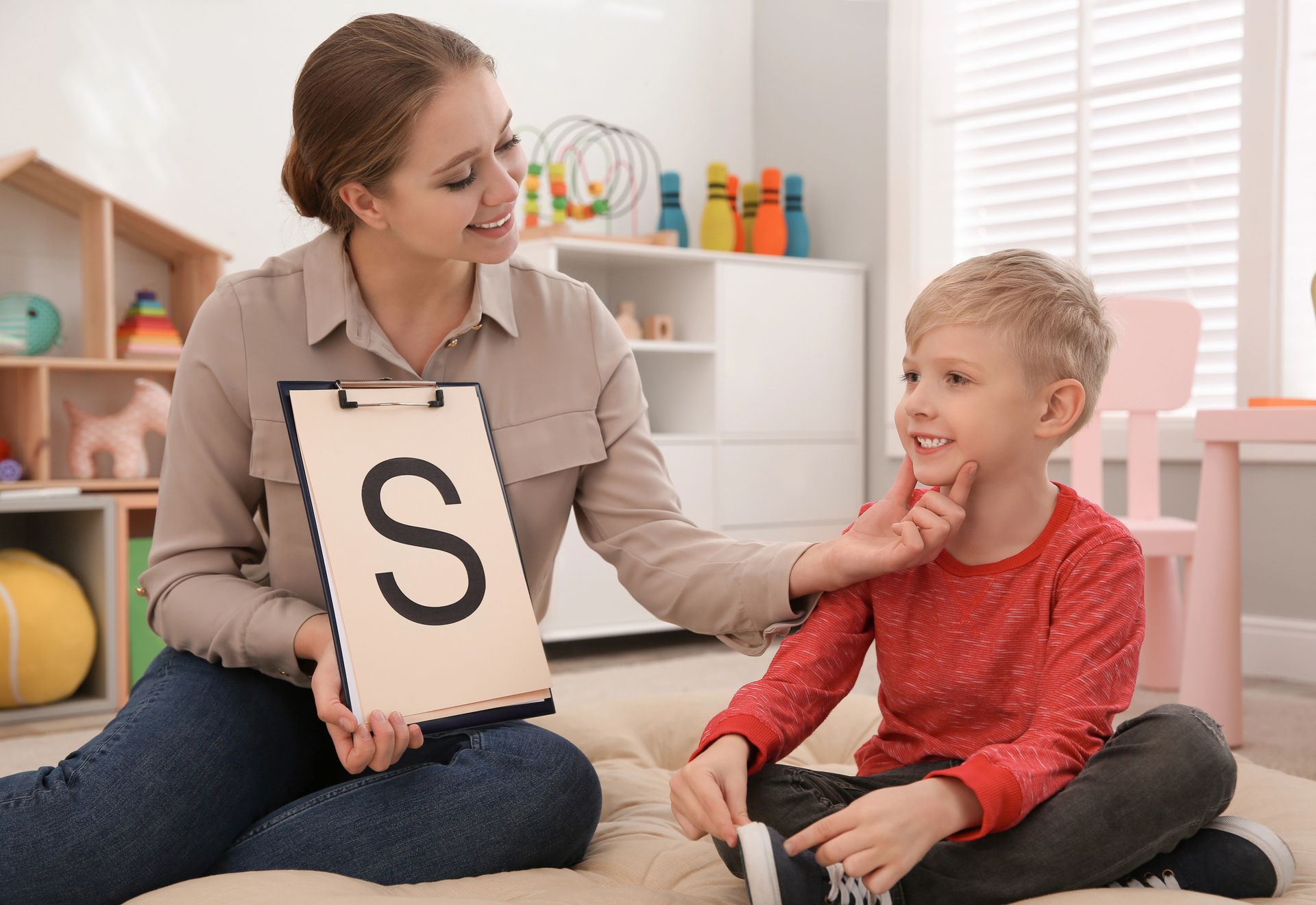 A woman is holding a clipboard with the letter s on it and talking to a young boy.
