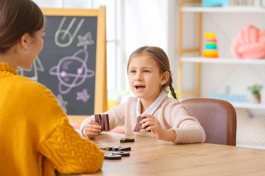 A little girl is sitting at a table talking to a woman.