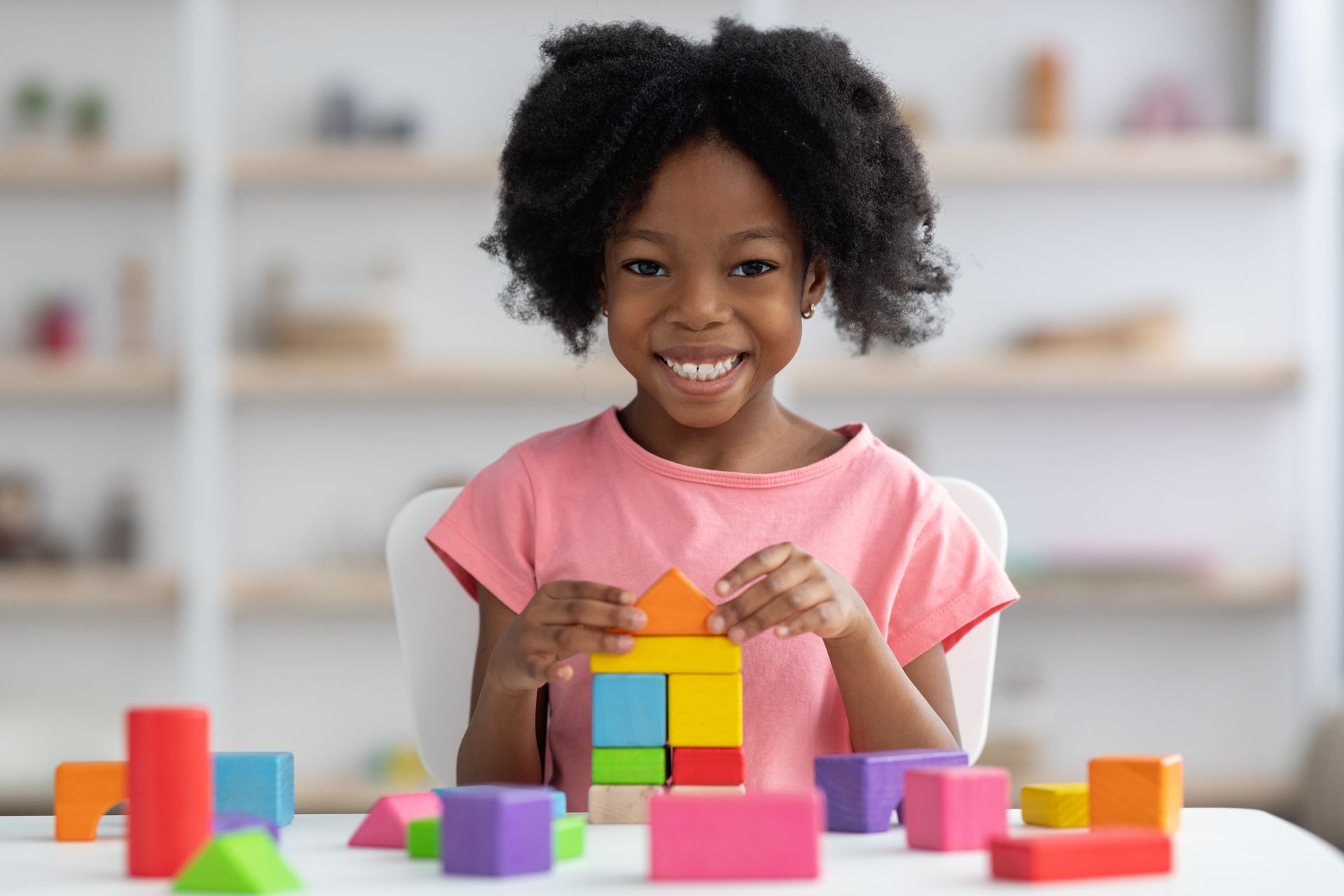 A little girl is sitting at a table playing with wooden blocks.