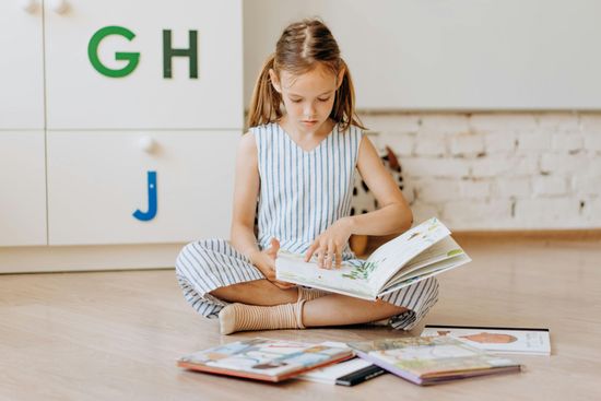 A little girl is sitting on the floor reading a book.