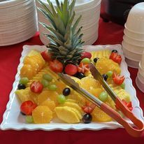 Fruit platter with pineapple, grapes, strawberries, and oranges, served with tongs.