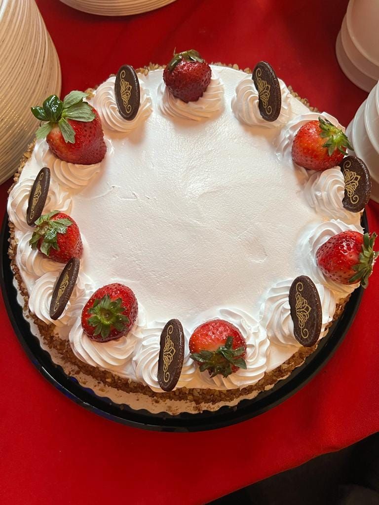Cake with white frosting, strawberries, and chocolate decorations. On a black platter, red surface.
