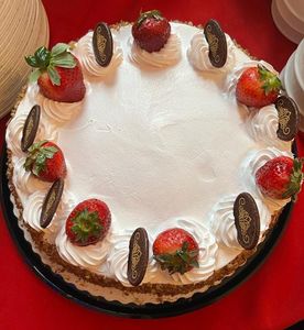 Round cake with white frosting, strawberries, and chocolate decorations.