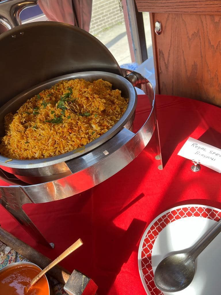 A buffet with rice in a warming dish on a red tablecloth. A plate and serving spoon are next to it.