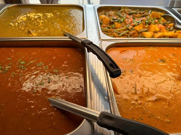 Four trays of prepared Indian food, various colors.