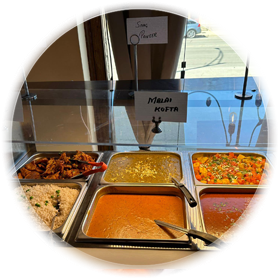 Indian food buffet with various dishes in metal trays.