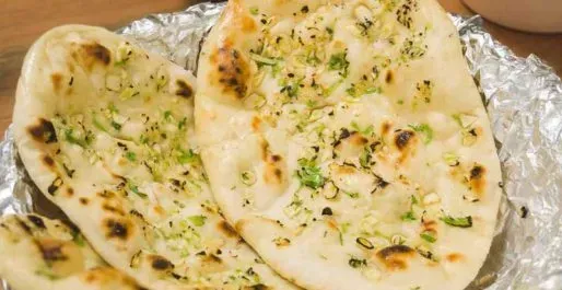 Two pieces of naan bread with garlic and herbs on foil.