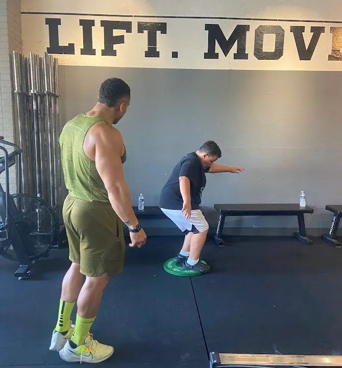 Man observing another man doing a balance exercise on a green disc at Iron Mile Fitness gym in Sacramento, CA