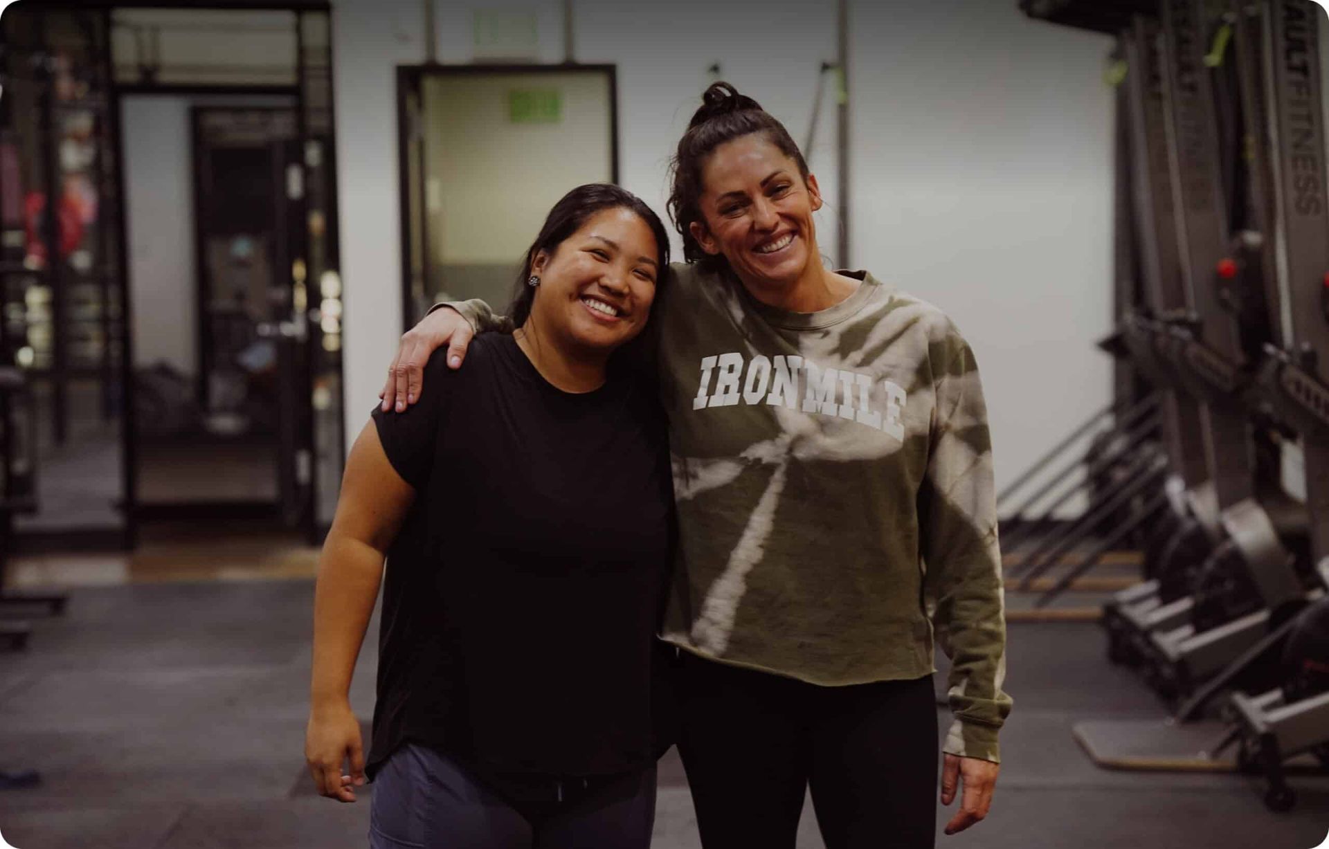 Two women smiling, arms around each other at Iron Mile Fitness gym in Sacramento, CA
