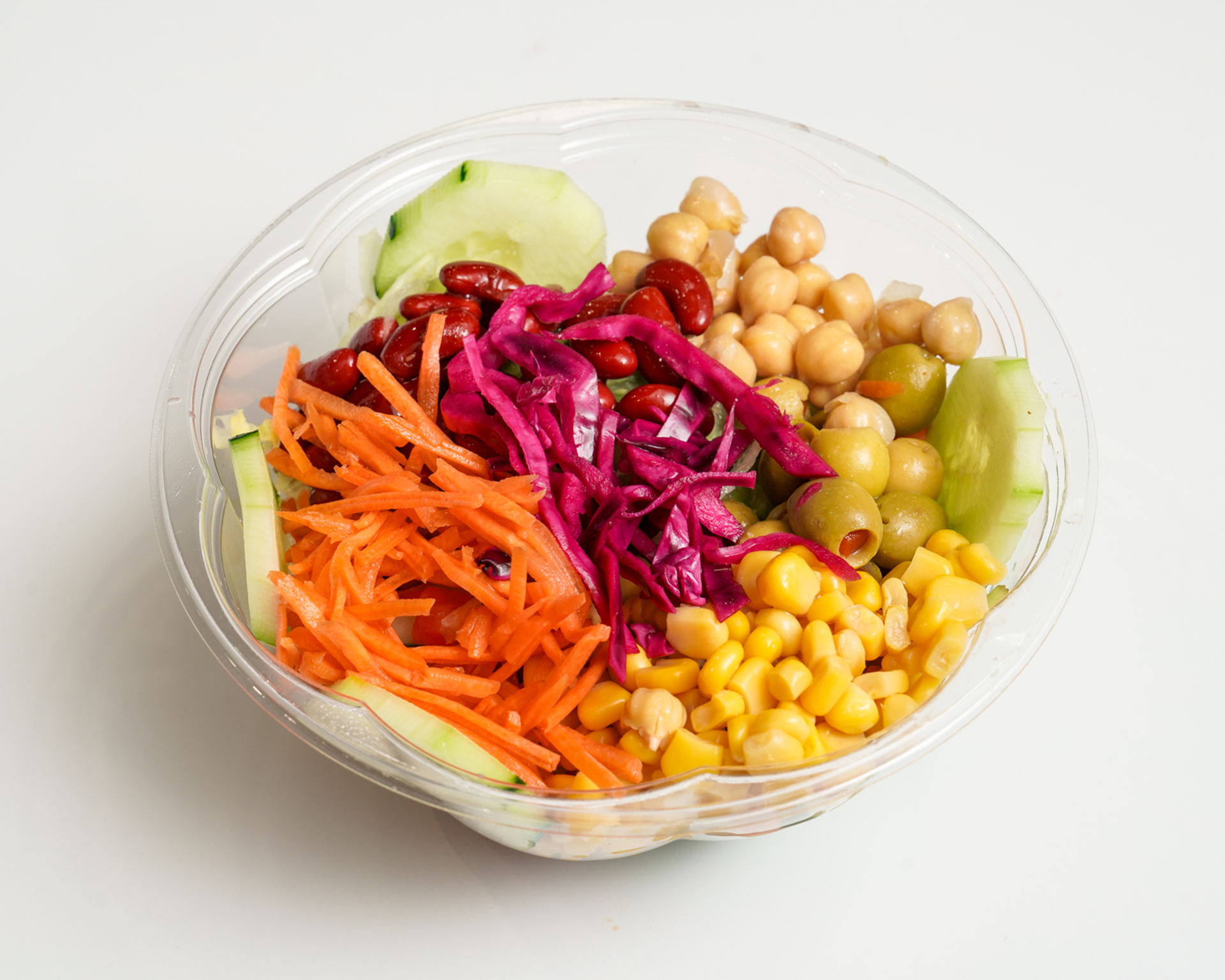 Salad bowl with shredded carrots, cucumber slices, red cabbage, chickpeas, corn, and olives.