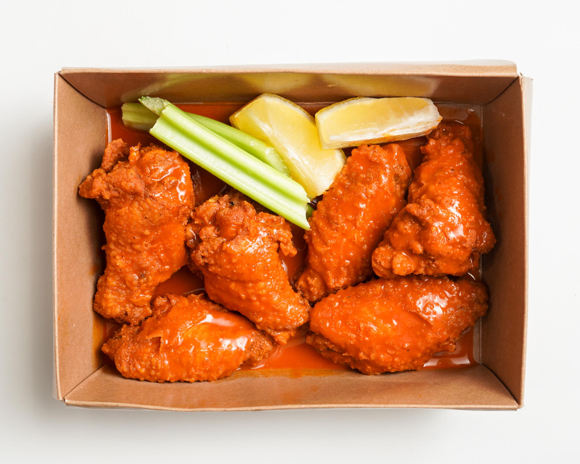 Buffalo chicken wings in a cardboard container with celery and lemon slices.