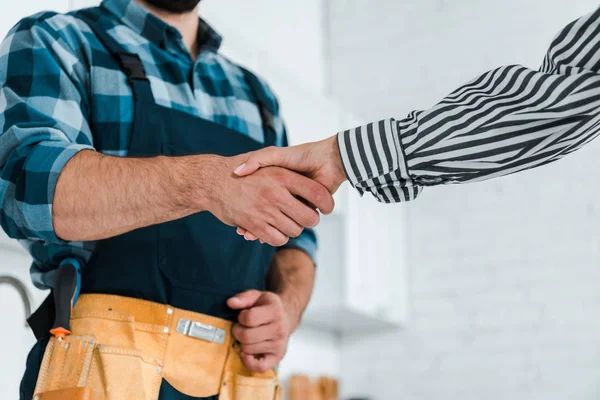 A man in an apron is shaking hands with another man.