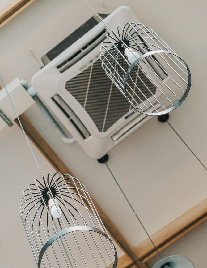 A bird cage hanging from the ceiling next to an air conditioner