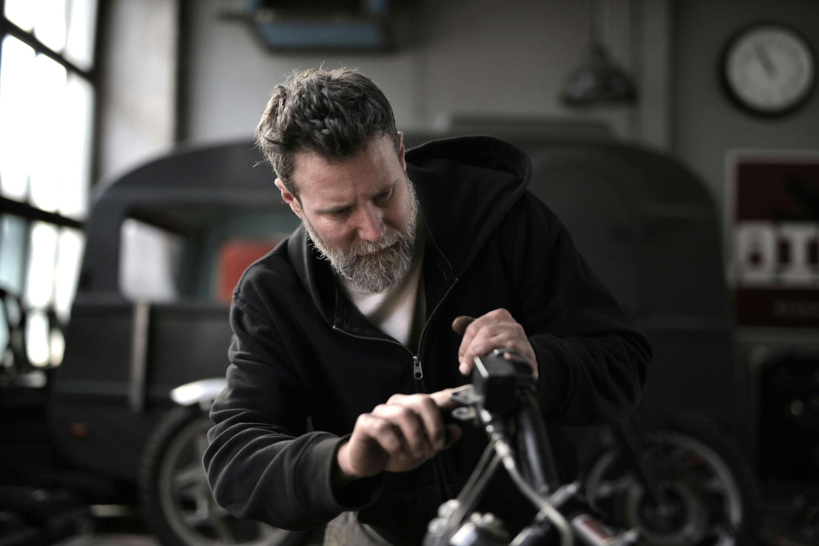 A man with a beard is working on a motorcycle in a garage.