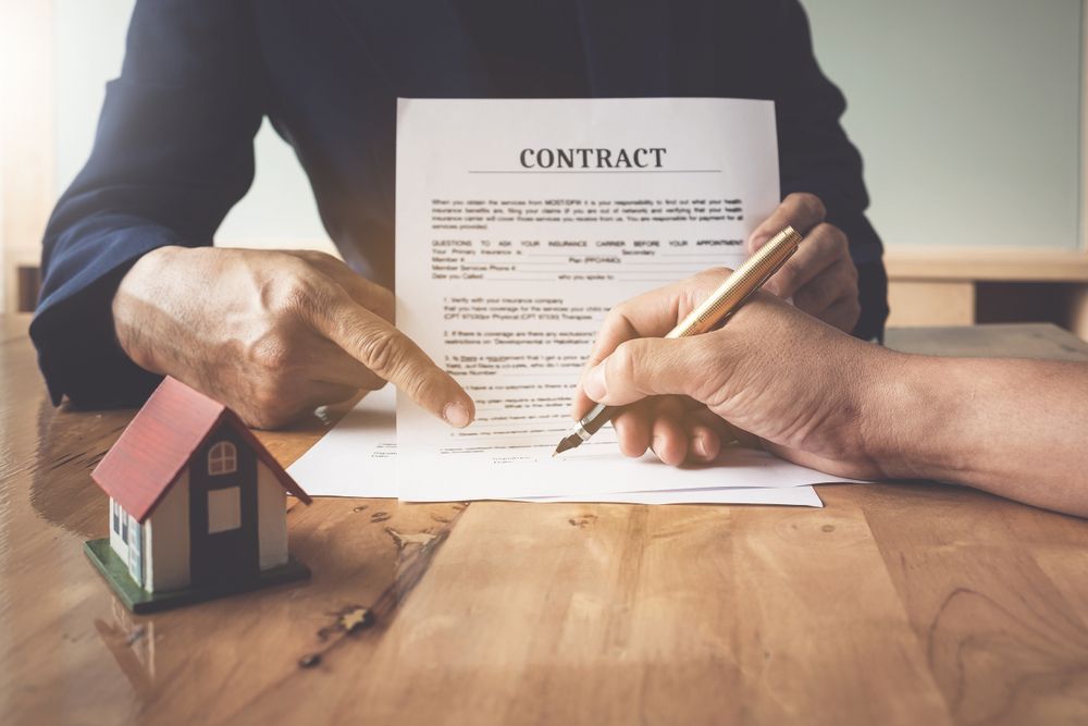 Hands Exchanging Contract Document With House Model Nearby