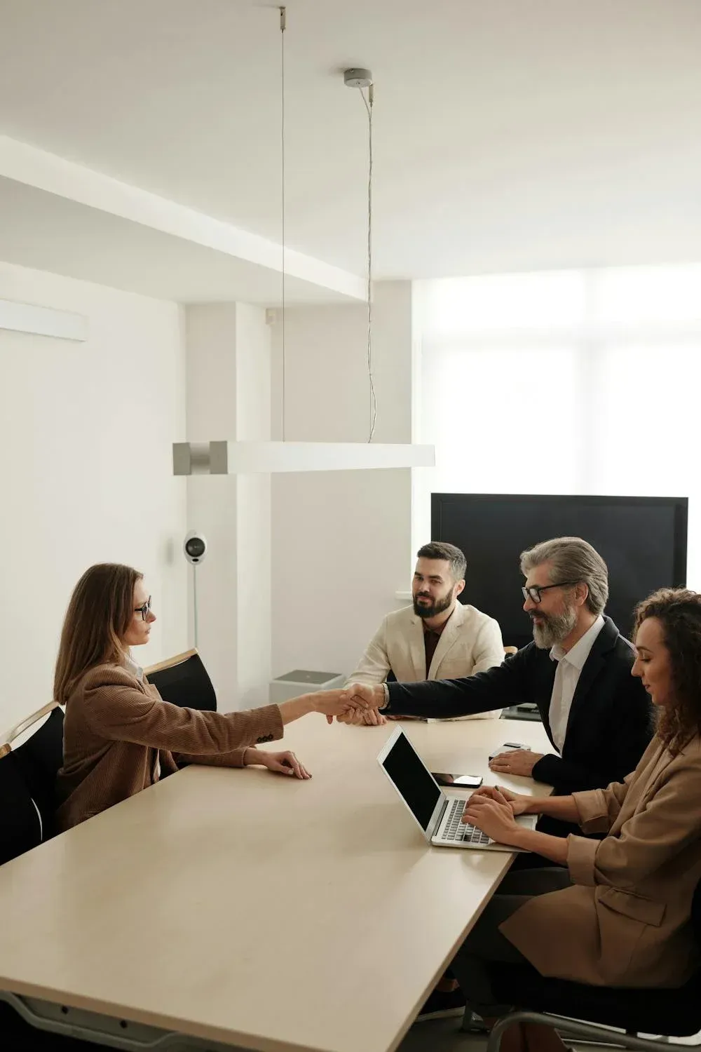 A group of people are sitting around a table shaking hands.