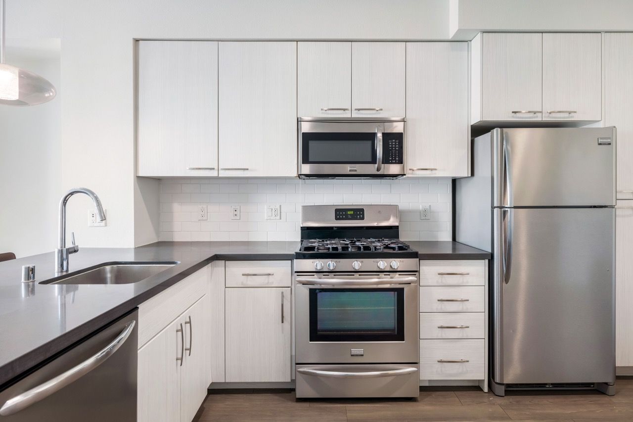 Angelene Apartments Modern kitchen with stainless steel fridge, microwave, gas range, and white cabinets.