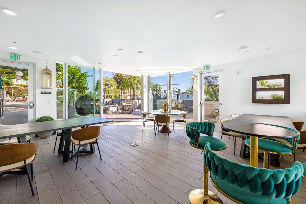 Angelene Apartments Interior community lounge with white walls, teal tufted chairs, and glass doors to an outdoor patio.