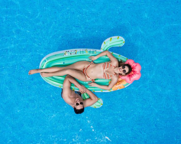 Couple relaxing on a cactus float in a blue pool.