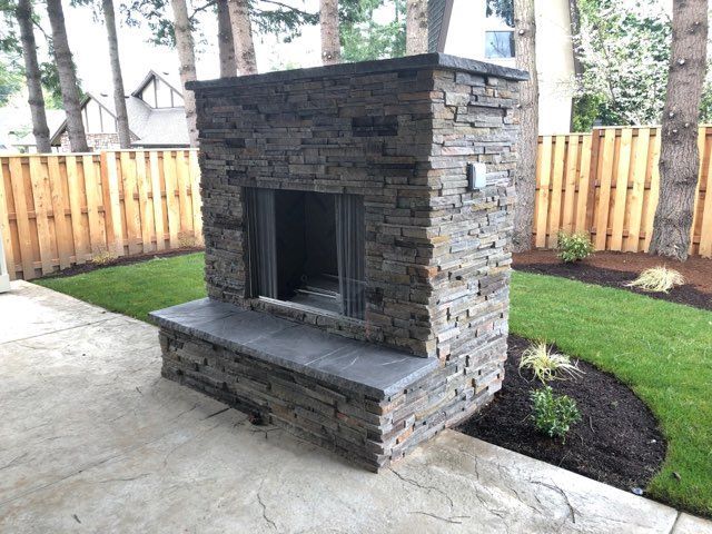 A stone fireplace in a backyard with a wooden fence in the background.