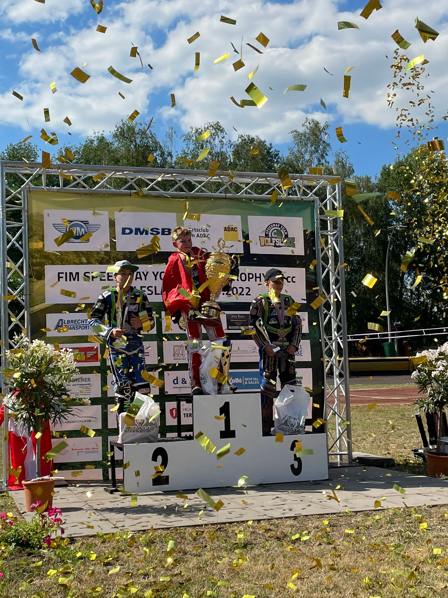 Eine Gruppe von Menschen steht auf einem Podium, um sie herum regnet Konfetti.
