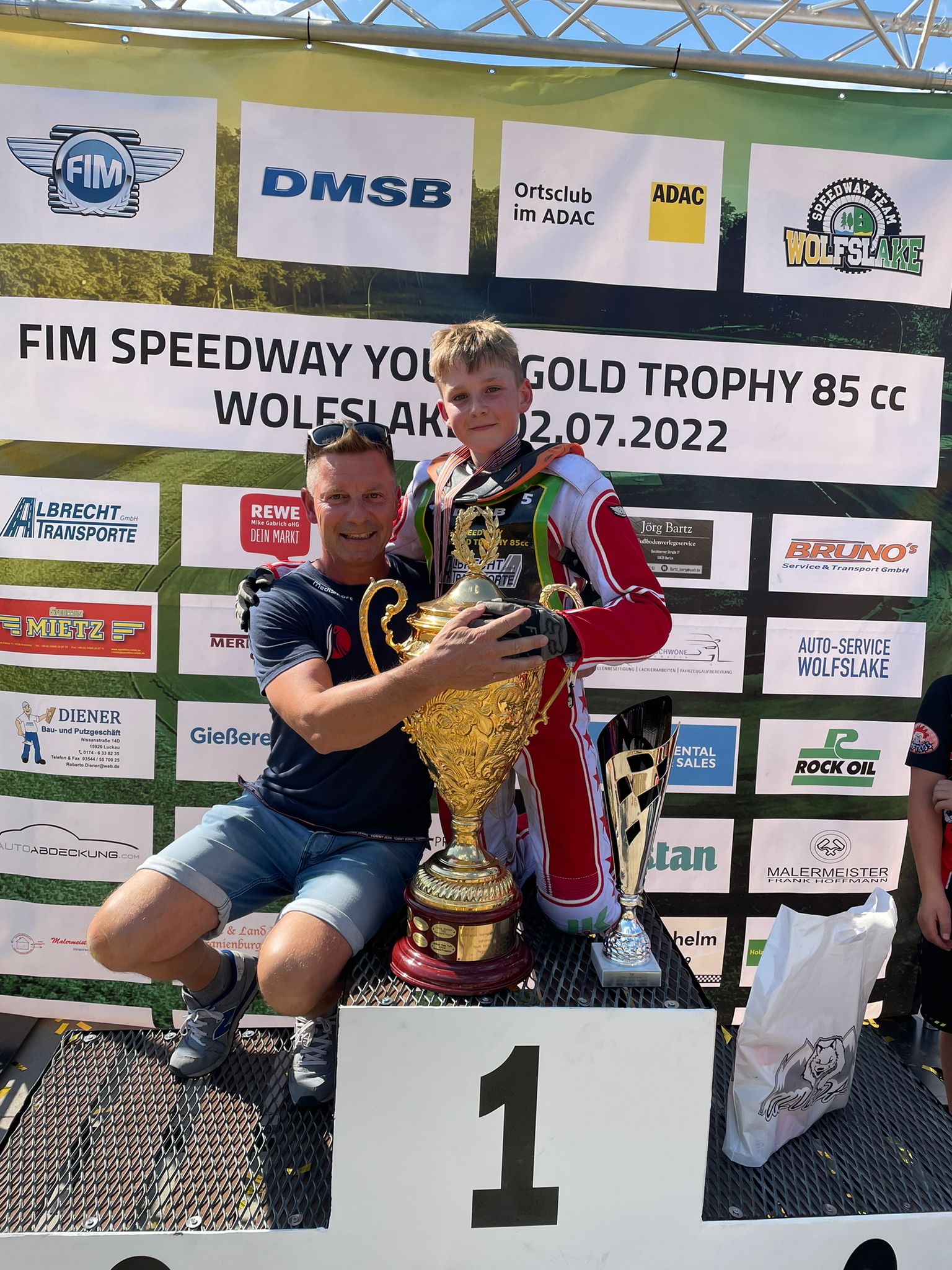 Zwei Männer stehen auf einem Podium und halten eine goldene Trophäe in den Händen.