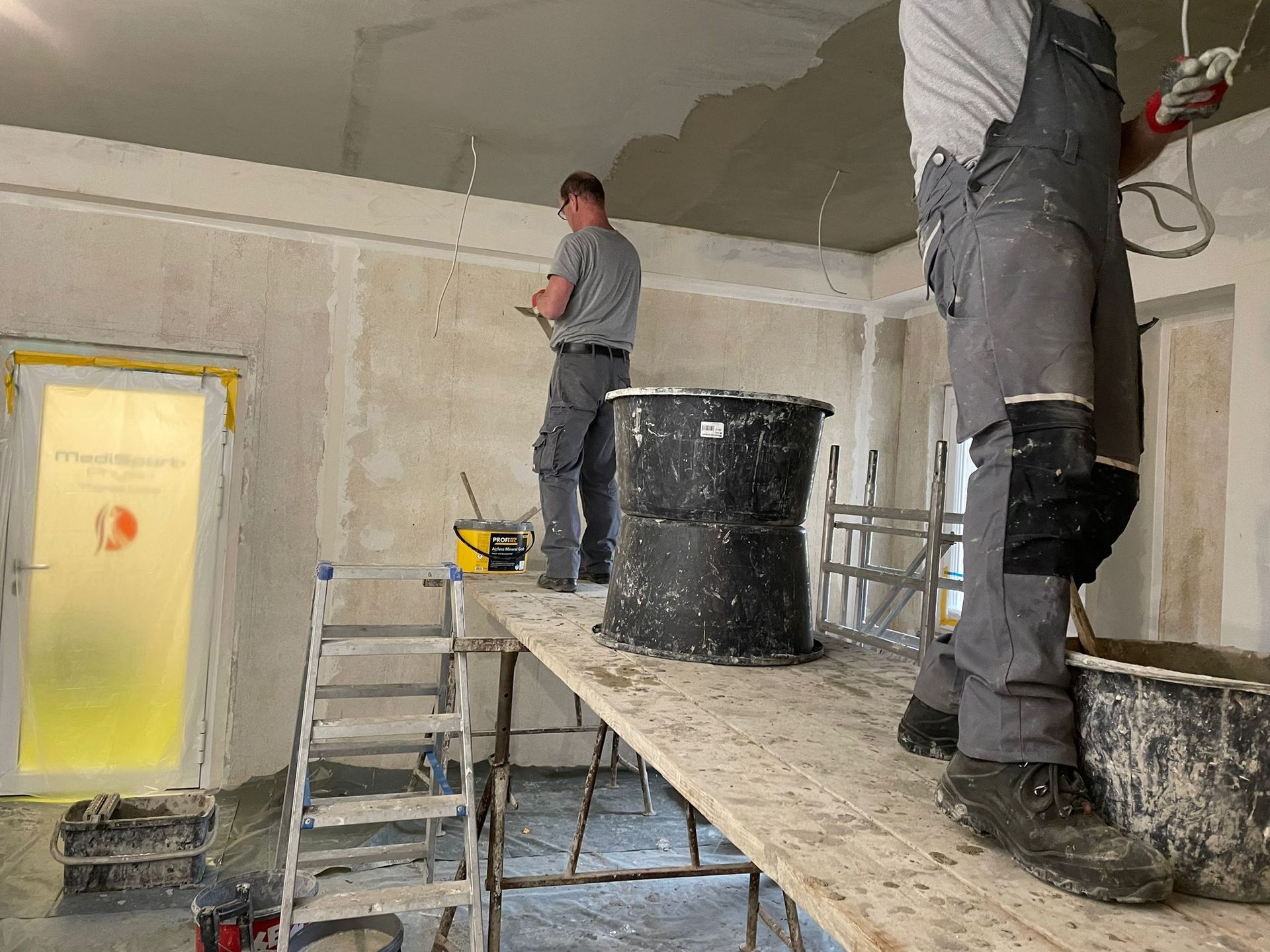 Zwei Männer arbeiten an einer Decke in einem Raum.