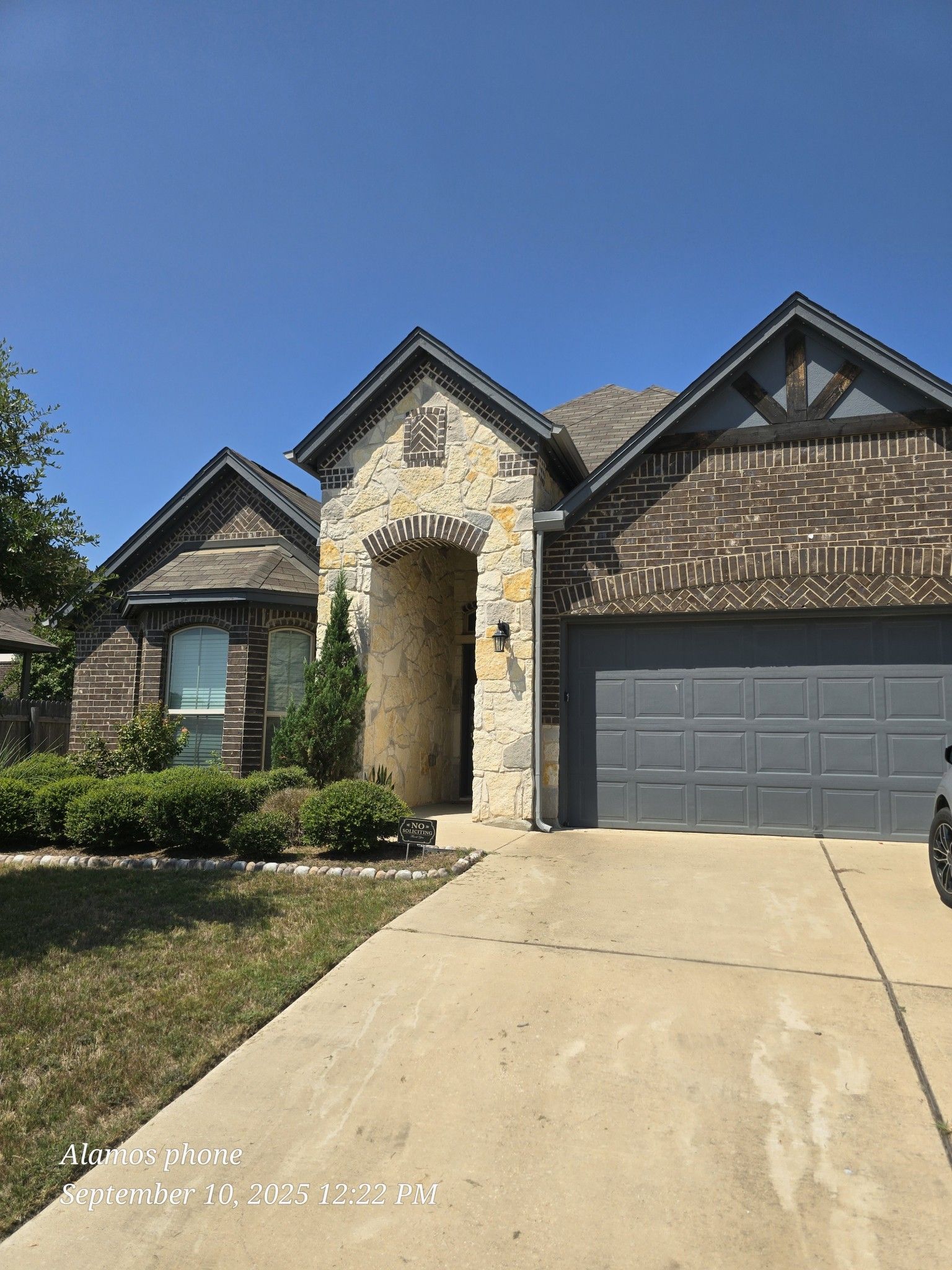 House exterior with stone archway, brick, grey garage door, and blue sky.